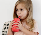 Child drinking at Ezpz Happy Cup & Straw in Coral - Available at www.tenlittle.com