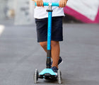 Child riding Micro Kickboard Maxi Deluxe Foldable LED Scooter - Bright Blue. Available at www.tenlittle.com
