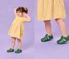 Split view of girl playing with bubbles and wearing Ten Little Splash Sandals 2 - Dino Green. Available at www.tenlittle.com